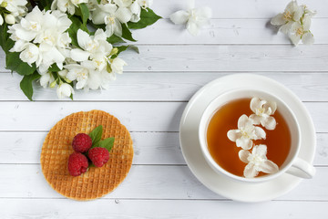 Tea Cup with Jasmine flowers and thin waffles with honey and raspberry on a light wooden background