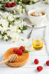 Tea Cup with Jasmine flowers and thin waffles with honey and raspberry on a light wooden background