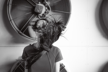 Young beautiful asian woman, on the background of industrial air conditioning system fans. Portrait of a girl with flying hair