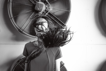 Young beautiful asian woman, on the background of industrial air conditioning system fans. Portrait of a girl with flying hair