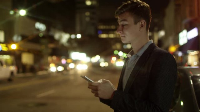 Young male is texting while standing on a street at night