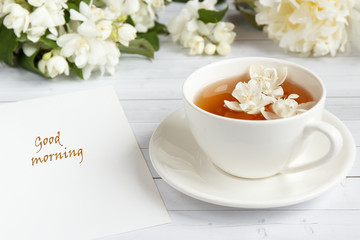 Cup of tea, pouring honey from a spoon in a jar, Jasmine flowers on a light wooden background. Copy space.