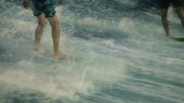 People practice surfing It's a aquapark, extreme athlete on shortboard, surfboard on wave attraction, happy sport people, close legs on board on vawe