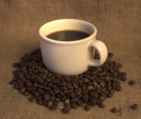A white coffee mug on coffee beans on a linen burlap.