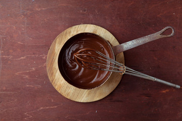 Melted chocolate swirl in pan with whisk on the wooden background