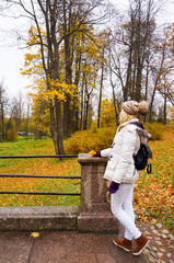 Fototapeta premium Young lady in a white jacket from the back looking at the autumn landscape in the Park. 