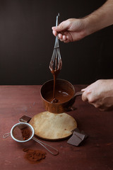 Male hands stirs melted chocolate swirl in pan on the wooden background