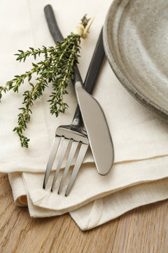 Simple, Natural Dinner Table Setting With Rustic, Casual Style Fork, Knife, Napkin And Plate, Accented With A Sprig Of Fresh Thyme Herbs