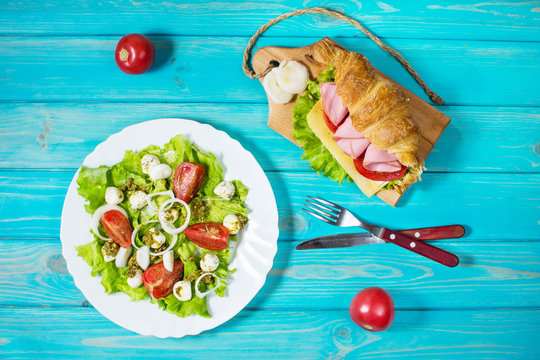 Light and hearty spring breakfast. Croissant with ham, cheese, fresh tomatoes and salad with Mozzarella on a wood table.