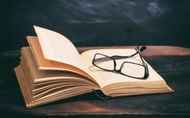 Old book and eye glasses on blackboard background