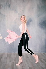 Attractive positive middle-aged blond woman wearing pink jacket and pants with trouser stripes with a beautiful smile posing against a receding wall looking directly at the camera. 