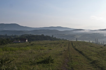 Romantic landscape with a lonely house. Misty mountains on the background