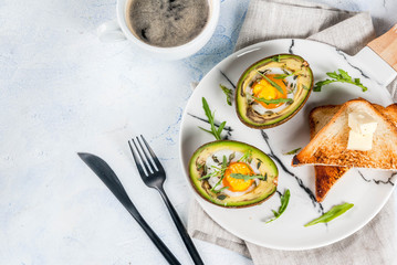 Healthy vegan breakfast. Diet. Baked avocado with egg and fresh salad from arugula, toast and butter. On a white marble plate, a light concrete table. A cup of coffee. Copy space top view
