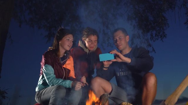 The young guys are sitting by the fire and doing a selfie photo