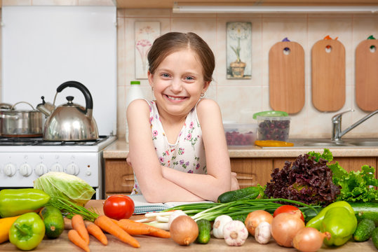 child girl with fruits and vegetables in home kitchen interior, read cooking book, healthy food concept