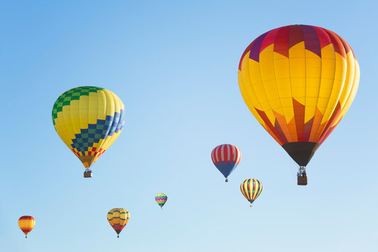 Multi colored hot air balloons in bright morning sky, group of balloons in sunny blue sky photographed from side 