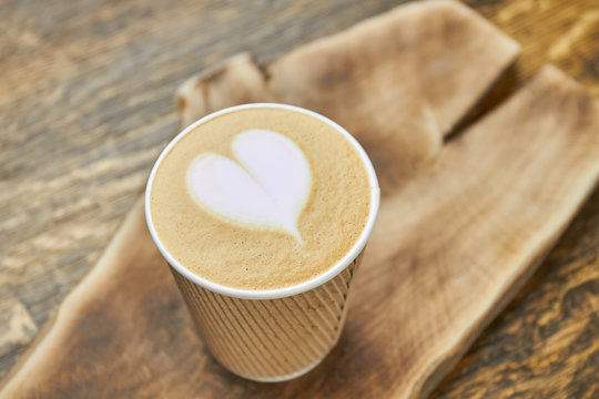 Heart latte art, paper cup. Coffee drink on blurred background. Love at first sip.