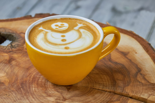Latte cup with snowman art. Coffee drink on wood board.