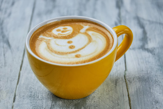 Coffee cup with snowman art. Latte on wooden surface.