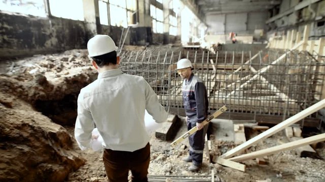 Professional engineers working together on construction site. Chief architect walking to worker standing near formwork of foundation. Builder with level listening to foreman waiting for instructions.