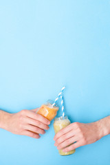 Woman hands holding smoothie shake against blue wall. Drinking healthy smoothie concept.