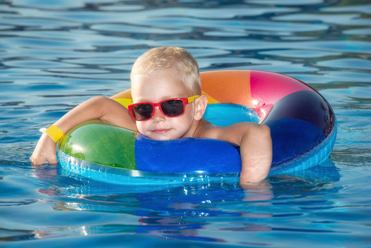 Happy little boy playing with colorful inflatable ring in outdoor swimming pool on hot summer day. Kids learn to swim. Child water toys. Children play in tropical resort. Family beach vacation