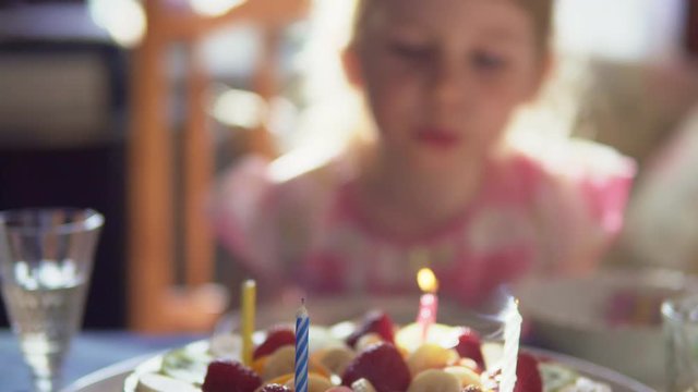 Little girl is blowing out candles on birthday cake and claping her hands