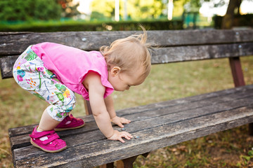 Fifteen months old baby girl climbing up the wooden bench in the park
