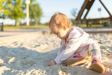 Fifteen months old baby girl playing in the sandbox in the sunset