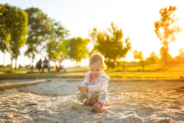 Naklejka premium Fifteen months old baby girl playing in the sandbox in the sunset
