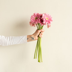 Woman's arm with joy wrist tattoo holding pink gerberas - love, gift concept