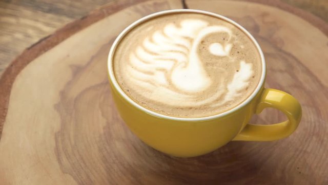 Swan latte art. Yellow cup on wooden board.