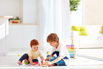 elder brother playing with little baby boy in colorful wooden bricks, at home