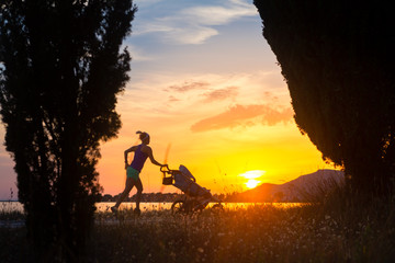 Silhouette of running mother with stroller enjoying motherhood at sunset landscape