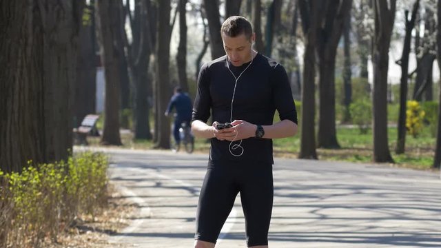 Young jogger listening to music with smartphone and hands free earphones pausing for texting then resuming running