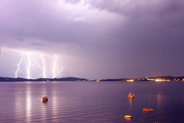 Naklejka na ściany i meble Beginnig of a storm in a sea with lightnings in purple sky. Yachts and boats parked in a bay.