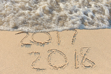 New Year 2018 sign in beach sand with frothy water edge