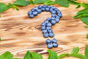 Question mark maked of fresh ripe natural blueberries with bright green spearmint frame on a brushed wooden background. Healthy diet  question concept