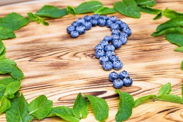Question sign maked of fresh ripe natural blueberries with bright green spearmint frame on a brushed wooden background. Healthy diet  question concept