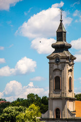 Orthodox church tower with clock under blue sky with clouds and flying bird