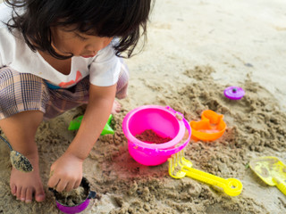 Little Asia girl sitting in the sandbox and playing whit toy shovel bucket and she was scooping in...