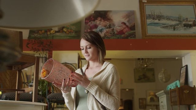 Medium slow motion panning shot of woman examining vase in antique store / Salt Lake City, Utah, United States