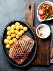 Grilled beef steak served on cast iron plate with tomato salad and potatoes balls. Barbecue, bbq meat beef tenderloin. Top view, slate background