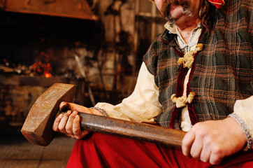 Blacksmith Kozak or a Cossack in Ukrainian national clothes with a hammer in the hands on the background of a blacksmith shop