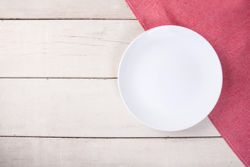 Top view of empty white plate put on red tablecloth and white wood table with space for copy.