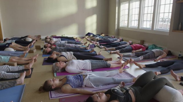 Wide slow motion zoom out shot of yoga students in corpse pose / Provo, Utah, United States