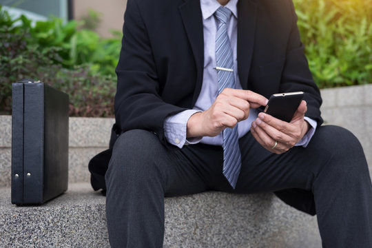business man wearing black suit and using modern smartphone in outdoor