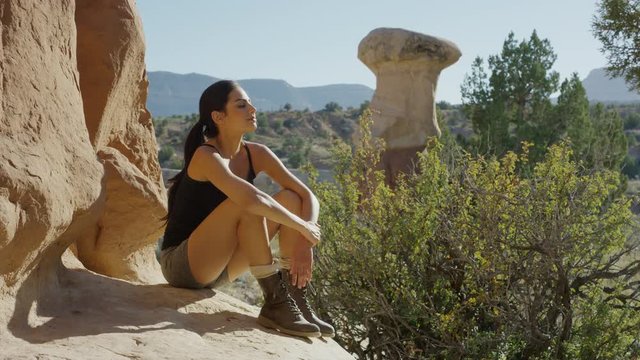 Medium panning shot of woman resting on desert rock / Escalante, Utah, United States