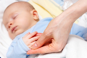 Mother holding hand of sleeping newborn baby