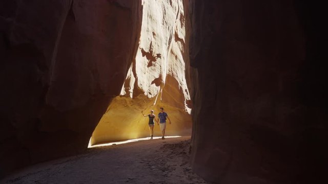 Wide panning shot of couple hiking in narrow canyon / Escalante, Utah, United States